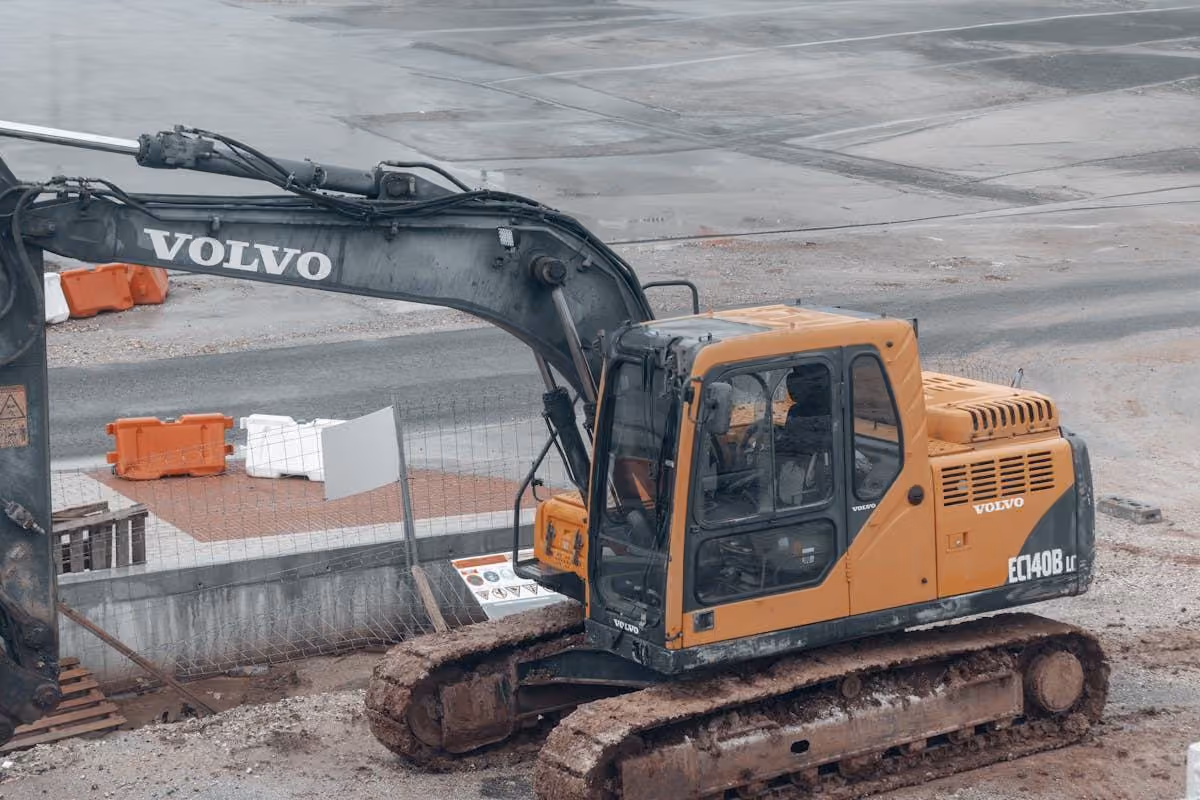 Excavator parked on a levelled site with sandy ground and a fence line behind