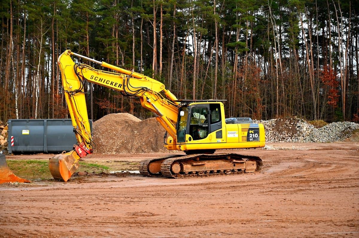 Yellow excavator working on a cleared building site with piles of earth and trees behind