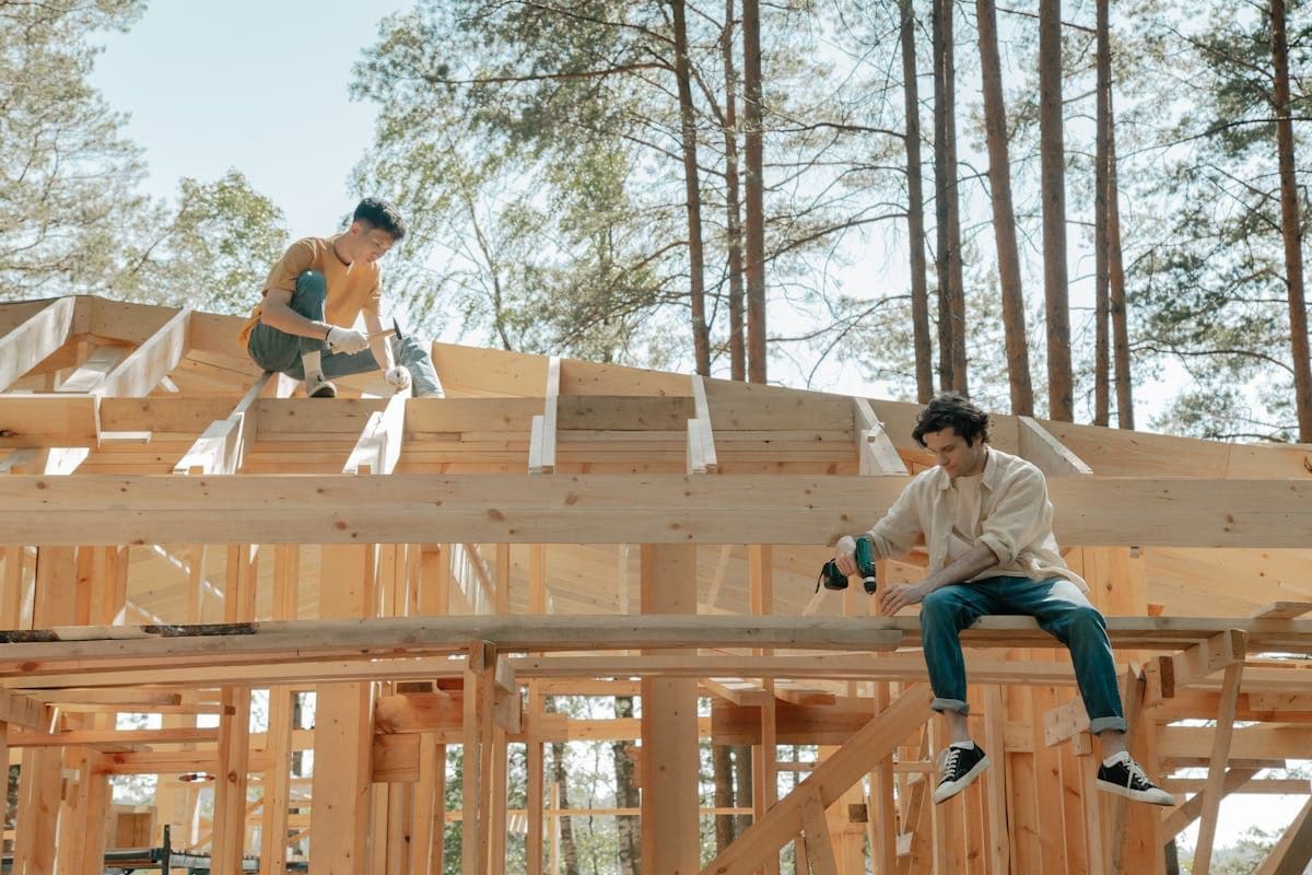 Two carpenters fixing rafters on an open roof structure against the sky