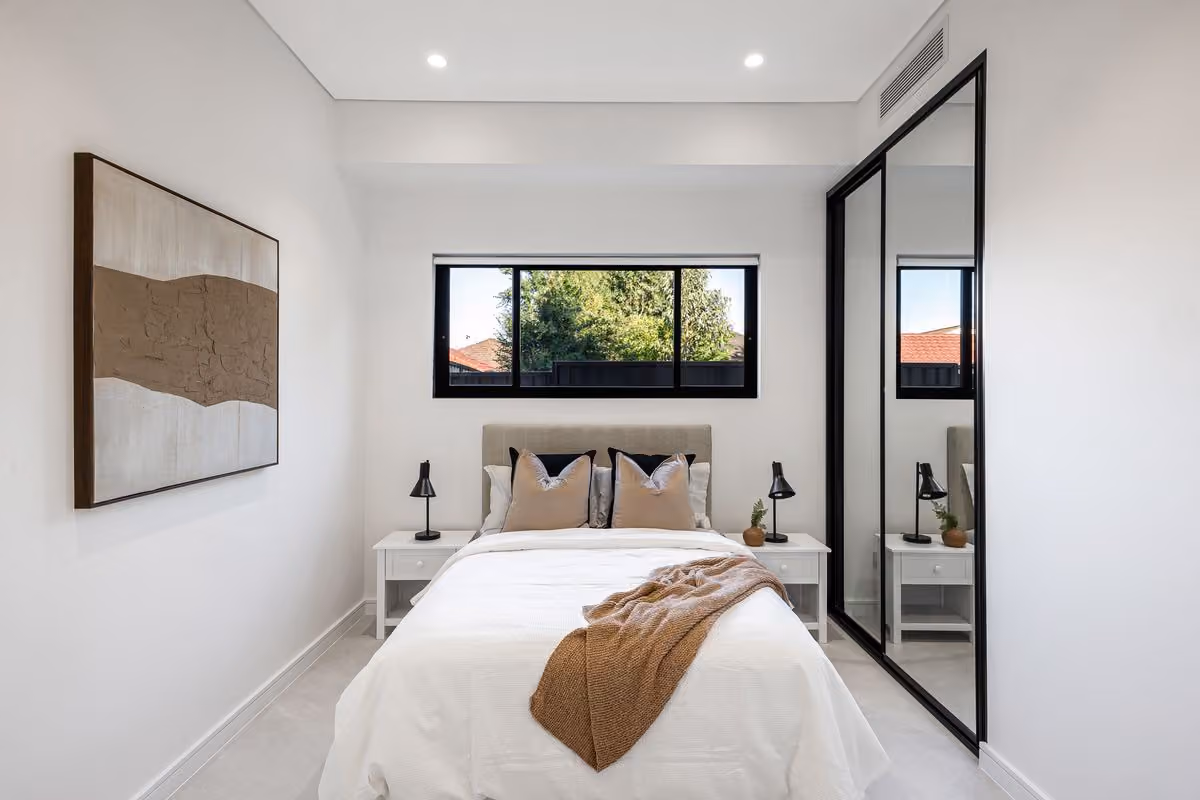 Guest bedroom with a mirrored robe, a padded bedhead and a window framed by trees