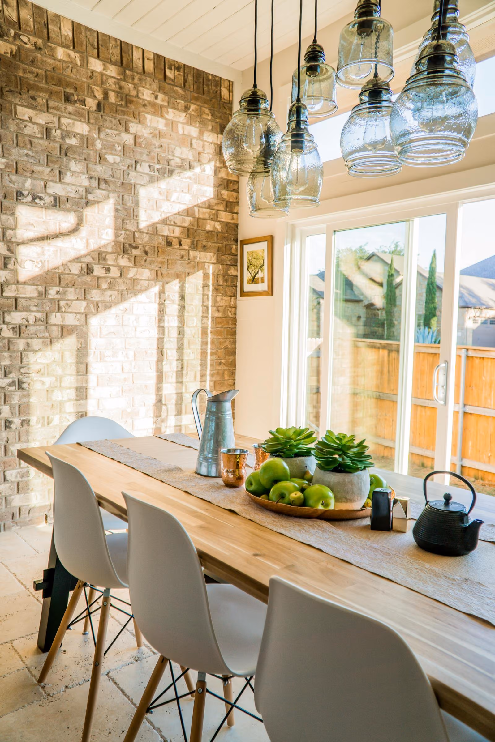 Sunlit dining table beside a bright window with plants and a jug
