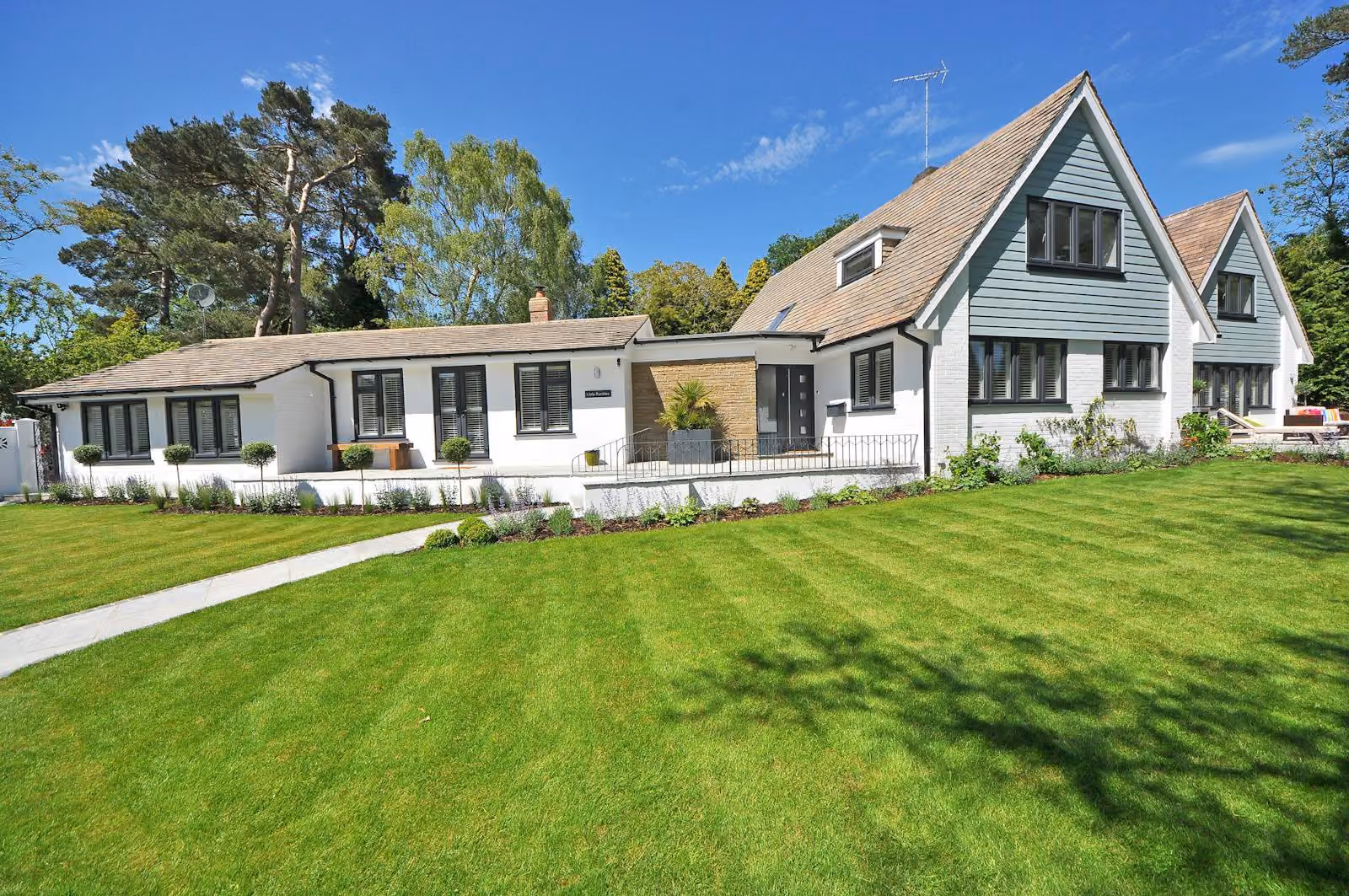 Two white-painted homes with steep gabled roofs set side by side behind a green lawn
