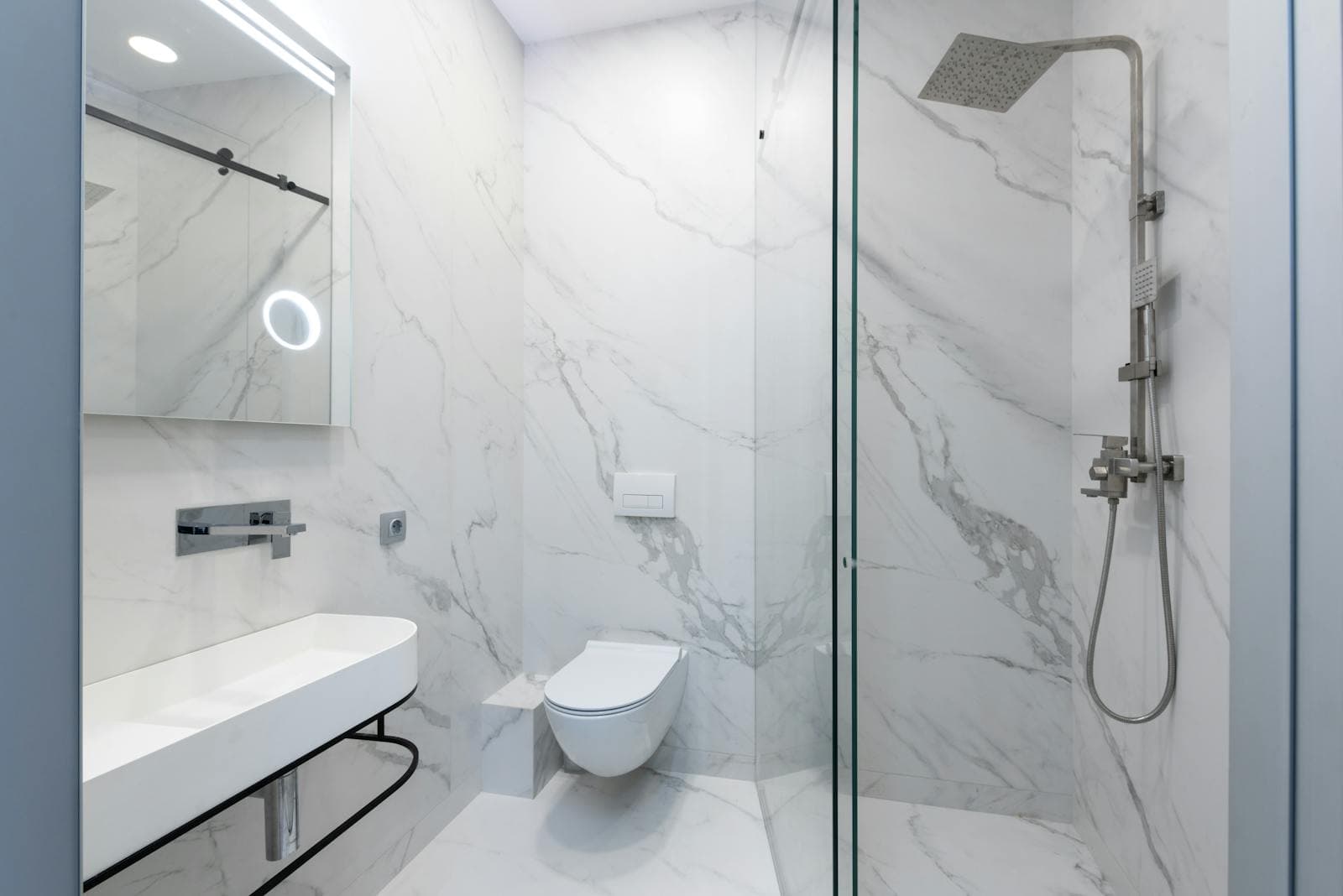 Marble-tiled walk-in shower with a frameless glass screen and a wall-hung toilet beside it