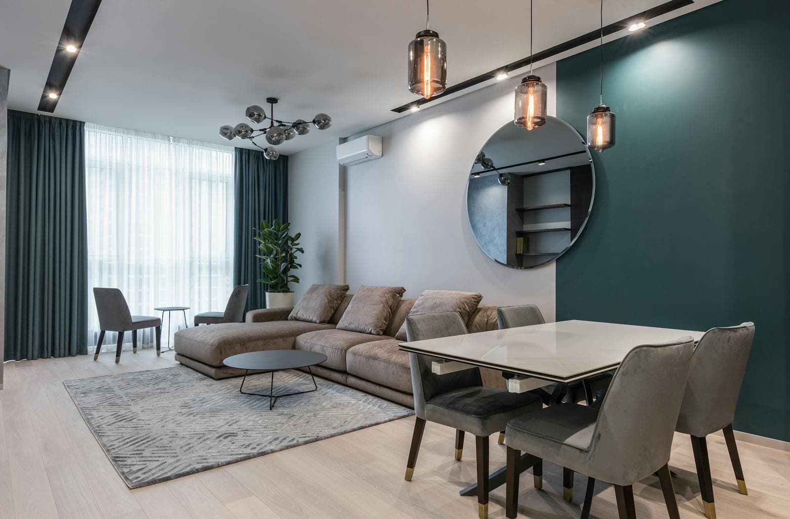 Modern apartment living and dining area with a teal feature wall, grey sofa and pendant lights