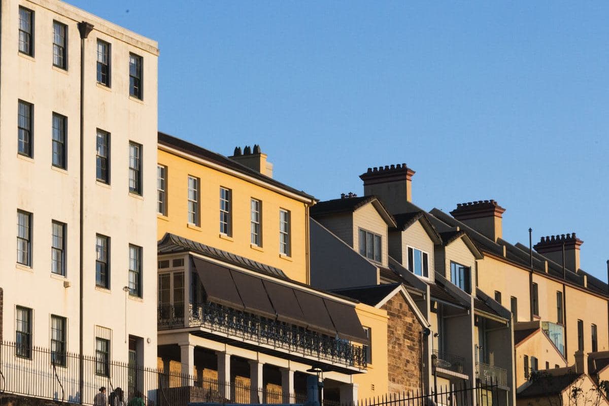 Row of historic rendered and sandstone-coloured buildings with balconies and chimneys against a blue sky