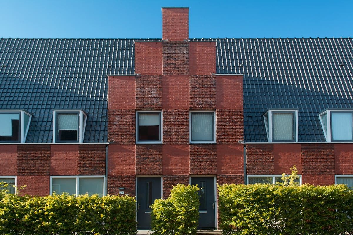 Red face brick building with a stepped gable, dark tiled roof and hedges along the front