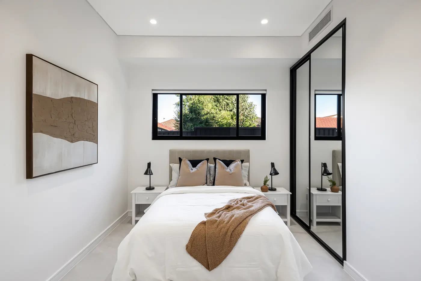 Compact bedroom with a mirrored robe, black-framed window and warm timber floor
