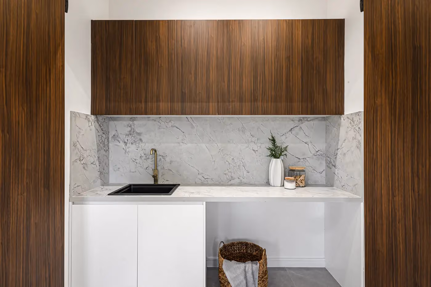 Walnut-look overhead cabinets above a marble-look splashback and a compact black sink